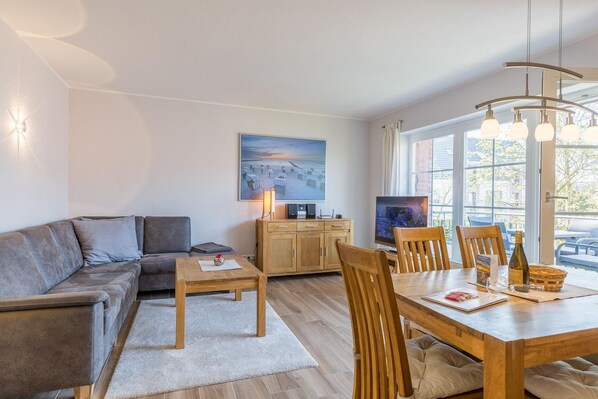 Un salon moderne comprenant un canapé, une table basse, une table à manger et des chaises. On y trouve également un téléviseur, un meuble et un tableau accroché au mur.
