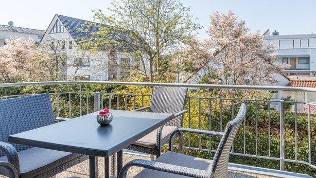 Un balcon doté de meubles en osier et d’une table, le tout entouré d’une rambarde en métal.