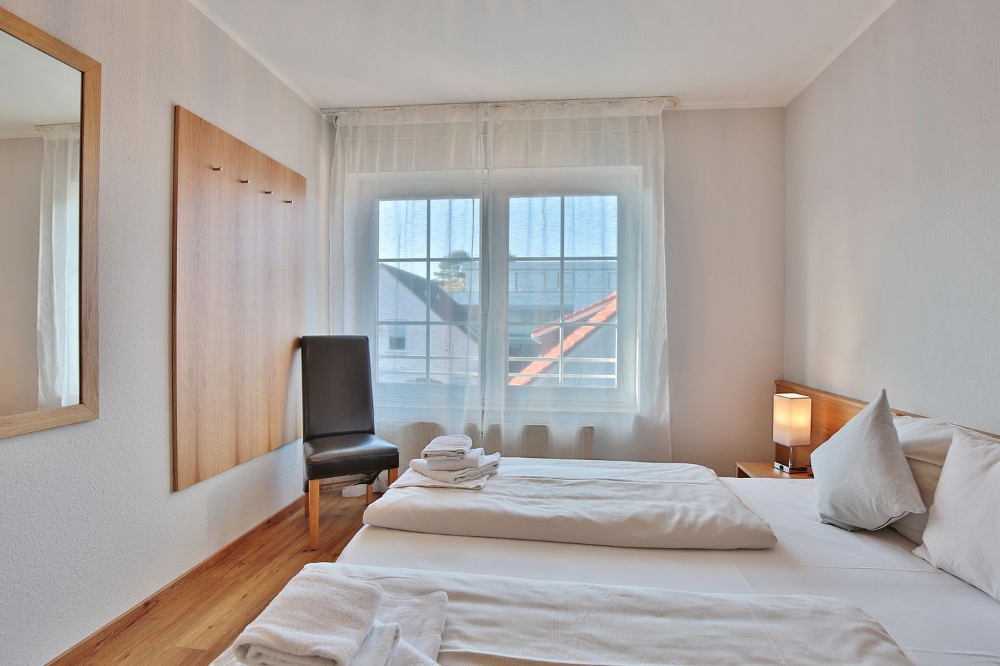 Habitación de hotel con cama, una silla, mesita de noche con lámpara y ventana con vista a un edificio.
