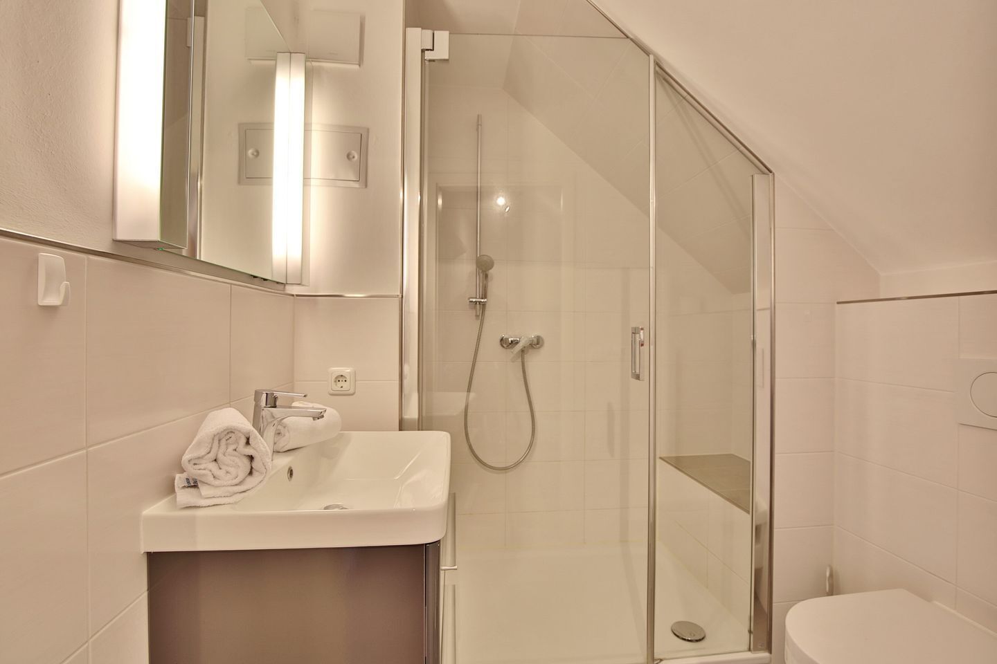 Een moderne badkamer met een douchecabine van glas, een witte wastafel en een spiegel erboven.