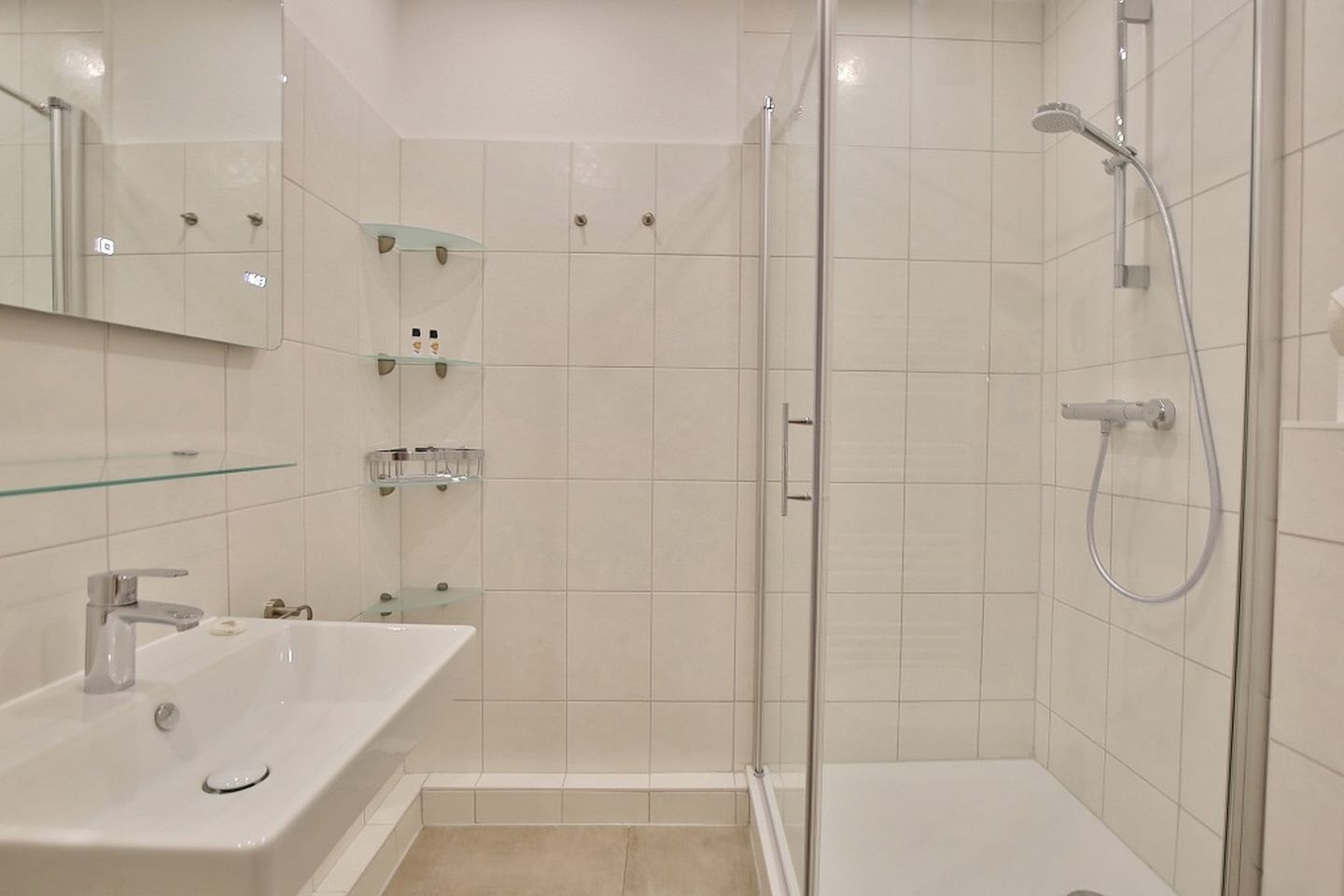 A modern bathroom with a glass shower enclosure, a sink with a mirror, and glass shelves.