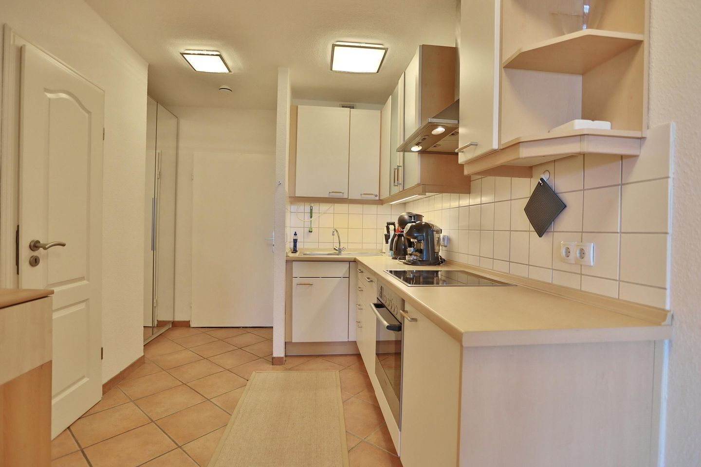 Una cucina compatta con mobili bianchi, forno integrato, lavello e macchina da caffè.