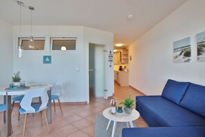 En moderne stue med en blå sofa, et spisebord med stole og et køkken i baggrunden.