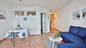 Una sala de estar moderna con un sofá azul, un comedor con sillas blancas y una cocina al fondo.