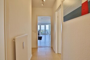 Un pasillo que conduce a una habitación con vistas, un radiador y una puerta con panel rojo y gris.