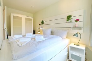 A hotel room with a neatly made bed, a bedside lamp, a small bedside table, and a wardrobe.