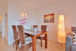 Un coin repas avec une table en bois, des chaises en osier, un vase de fleurs, un tableau et un grand lampadaire.
