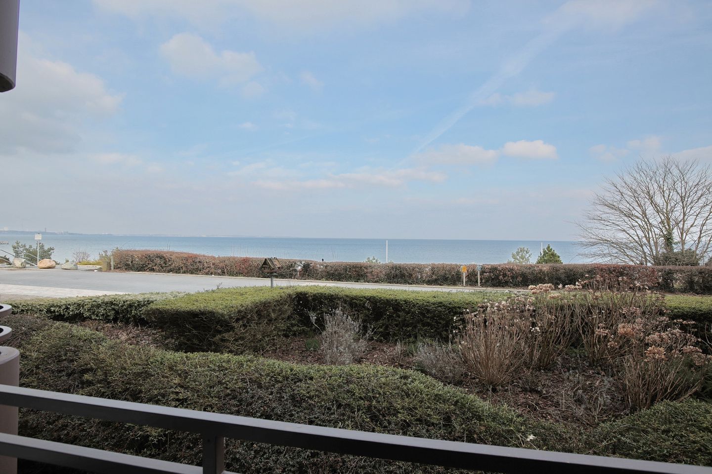 Blick auf die Küste vom Balkon aus, mit blauem Himmel, einer Straße und weiter Wasserfläche im Hintergrund.