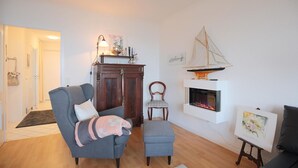 Una sala de estar con chimenea, un sofá, una silla y una mesita con un cuadro.