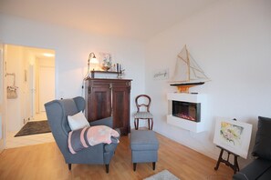 Una sala de estar con chimenea, un sofá, una silla y una mesita con un cuadro.