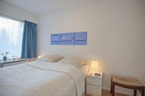 Un dormitorio con cama, mesitas de noche, una silla y decoración en la pared.
