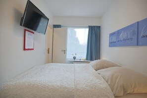 A hotel room with a bed, a flat-screen TV mounted on the wall, a window with curtains, and a wall with a framed certificate.