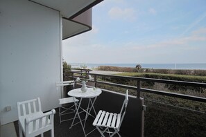 A balcony with white chairs and a table, overlooking a coastal landscape with a clear sky.