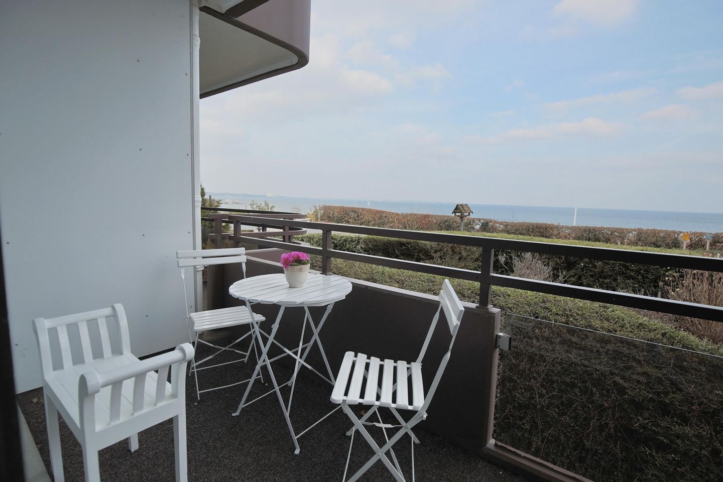 Ein Balkon mit Tisch und zwei Stühlen mit Blick auf eine Küstenlandschaft.