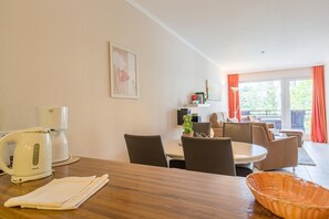 A dining area with a wooden table, chairs, a coffee maker, a plant, and a window with curtains.