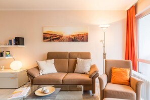 A modern living room with a sofa, armchair, and a painting on the wall.