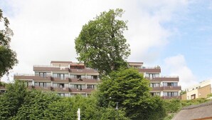 A multi-story building with balconies, surrounded by trees and a clear sky.