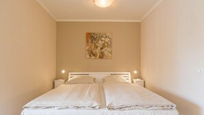 A neatly made bed with two pillows and a headboard, a bedside lamp, and a painting on the wall.