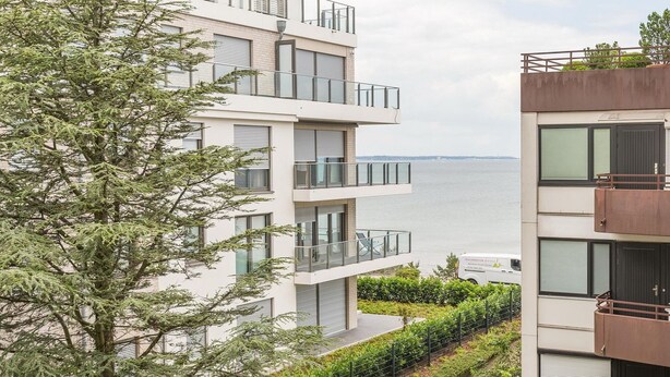 A modern multi-story residential building with balconies overlooking a body of water.