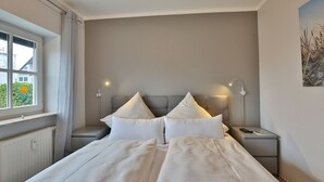 Ein ordentlich eingerichtetes Schlafzimmer mit einem Bett, zwei Nachttischen, einem Fenster und einem Beistelltisch.