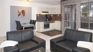 A modern living room with two black leather sofas, a glass coffee table, and a dining area with a glass table and chairs. A kitchen with white cabinets and stainless steel appliances is visible in the background. - Baltic Sea view apartment 3 - Baltic Sea view (Scharbeutz)
