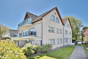 Un immeuble résidentiel à plusieurs étages, doté d’un design moderne, avec des balcons, de grandes fenêtres et un jardin bien entretenu.