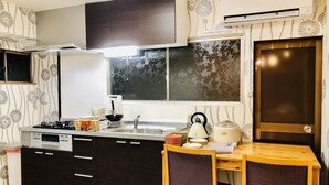A compact kitchen with dark cabinets, a gas stove, a sink, and a dining area with two chairs. - Art House  (東大阪市足代)