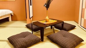 A traditional Japanese room with tatami flooring, a low table with cushions, a vase with flowers, and a sliding door. - Art House  (東大阪市足代)