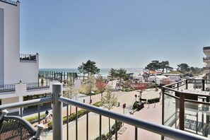 Un balcón con vista a la playa, un estacionamiento y un edificio con fachada de vidrio.