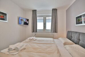 Habitación de hotel con una cama, ventana con cortinas, radiador y dos cuadros en las paredes.