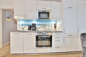 Una cocina moderna con armarios blancos, horno integrado y cafetera.