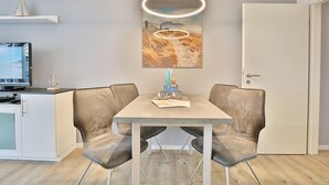 A modern dining area with a table and two chairs, a television on a cabinet, and a framed artwork above the table. - Seebrücke Appartement 2 - Seebrücke (Scharbeutz)