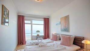 A hotel room with a large bed, two pillows, a bedside lamp, a window with curtains, and a painting on the wall.
