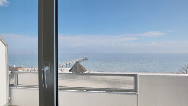 A view of a coastal area with a pier extending into the sea, a beach, and a building with a balcony.
