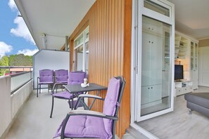 A balcony with purple chairs and a table, a sliding glass door, and a TV in a white cabinet. - Strandperle 201 Apartment - Strandperle (Scharbeutz)