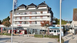 A multi-story building with a restaurant named 'JANNYS' on the ground floor, a visible staircase, and a flagpole with flags. - Strandperle Apartment 201 - Strandperle (Scharbeutz)