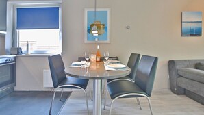 A modern kitchen with a dining area, a gray sofa, and artwork on the walls. - Strandperle Apartment 201 - Strandperle (Scharbeutz)