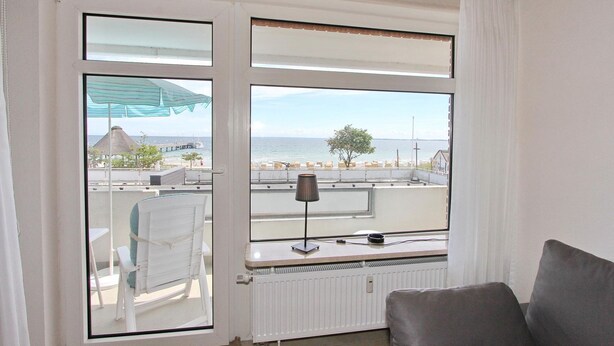 A balcony with a view of the sea, a chair, a table, and a lamp. - Strandperle Apartment 107 - Strandperle (Scharbeutz)