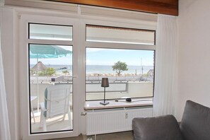 A balcony with a view of the sea, a chair, a table, and a lamp.