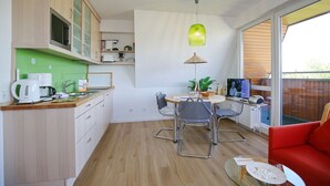 A compact kitchen with a dining area, a red sofa, and a large window. - Strandperle Apartment 403 - Strandperle (Scharbeutz)