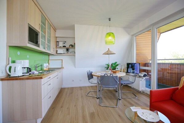 A compact kitchen with a dining area, a red sofa, and a large window.