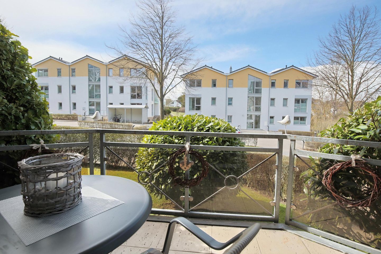 Un balcon avec une table et des chaises, donnant sur une rangée d’immeubles d’appartements modernes.