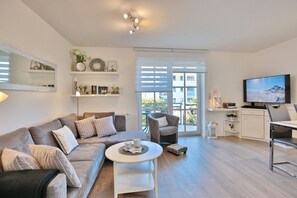 A modern living room with a sofa, a coffee table, a TV, and a balcony with a view.