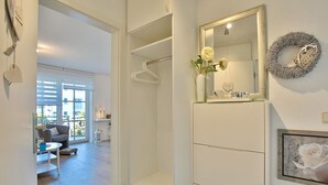 Una habitación moderna y bien iluminada, con un espejo grande, un armario blanco y un cuadro con una rosa blanca.