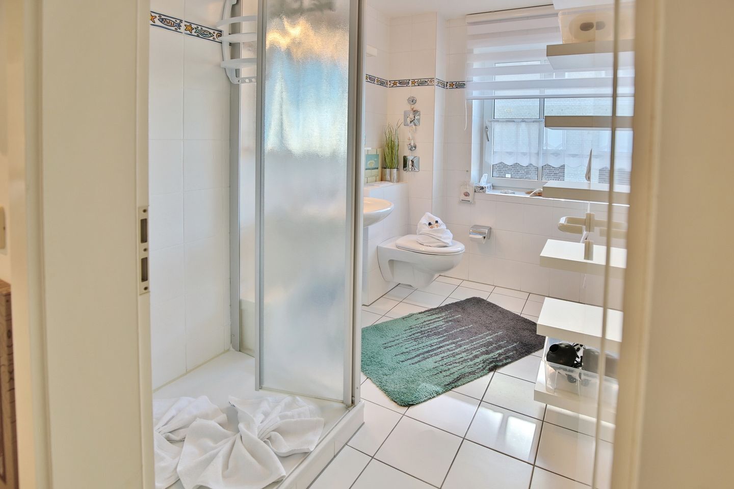 Un baño con cabina de ducha de vidrio, inodoro, lavabo y ventana.