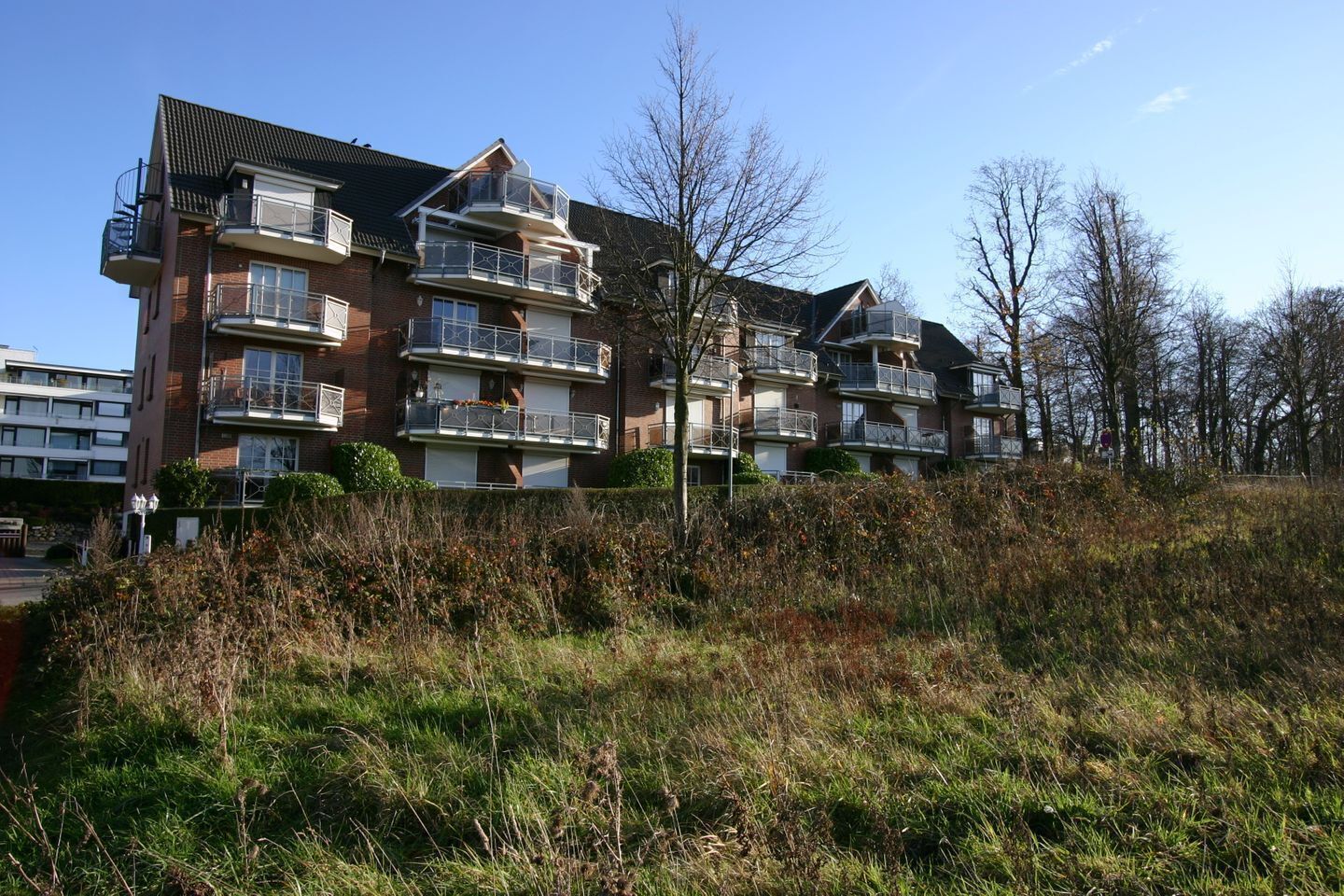 Un immeuble résidentiel à plusieurs étages, doté de balcons, d’une façade en briques et d’un parterre gazonné.