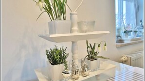 Un atril blanco de tres niveles con plantas en macetas y adornos decorativos.