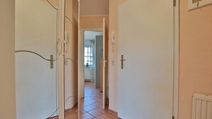 A narrow hallway with tiled flooring, white doors, and a radiator on the right wall.
