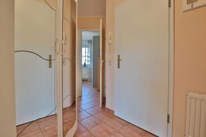 A narrow hallway with tiled flooring, white doors, and a radiator on the right wall.
