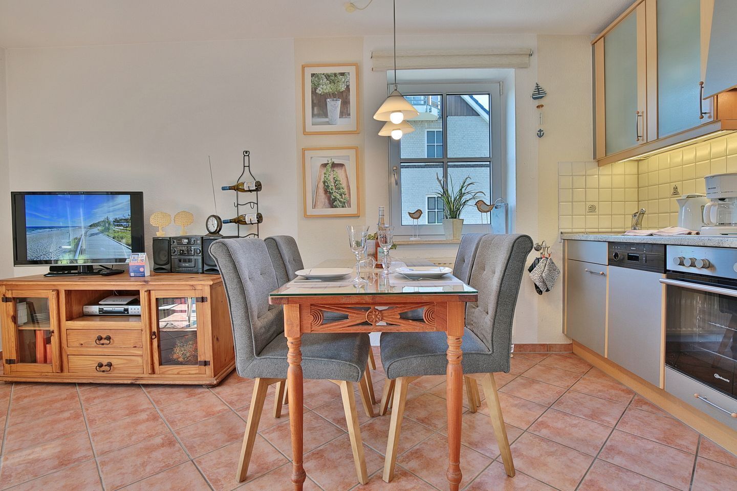 Eine kompakte Küche mit Essbereich, ausgestattet mit einem Holztisch, grau gepolsterten Stühlen, einem Einbauofen und einem Fernseher auf einer Holzkommode.